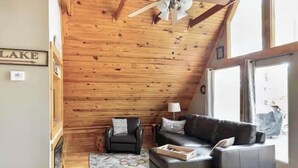 Una habitación acogedora con techo de madera, chimenea, sofá, sillón y un ventanal grande.