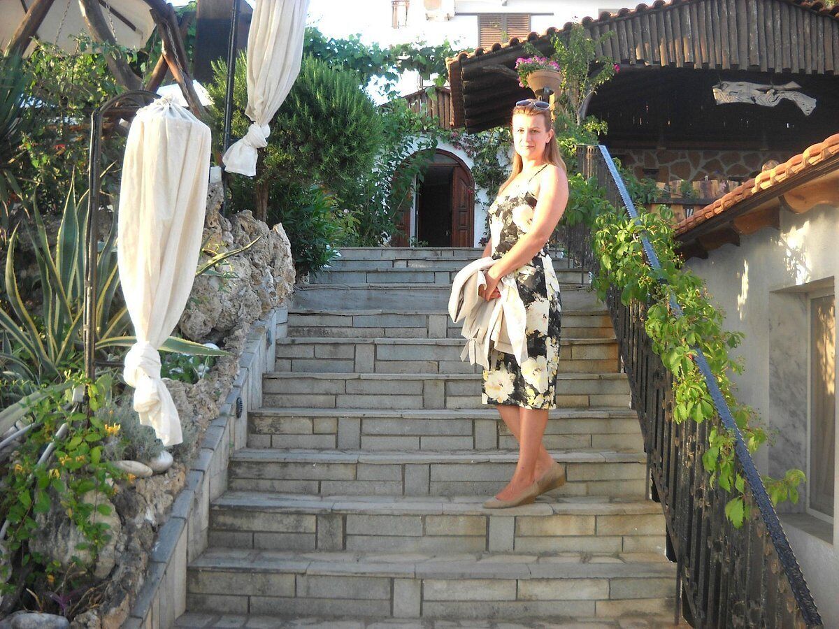 A person standing on stone steps with a white cloth draped over them, leading to a building with a wooden roof and a stone wall.
