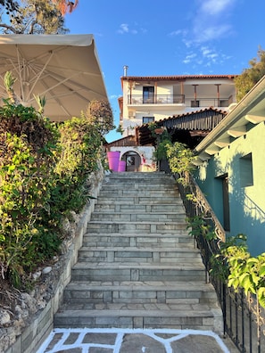 A stone staircase leading to a building with a balcony, surrounded by greenery and a clear sky. - HOTEL ESPERIA (Thasos)
