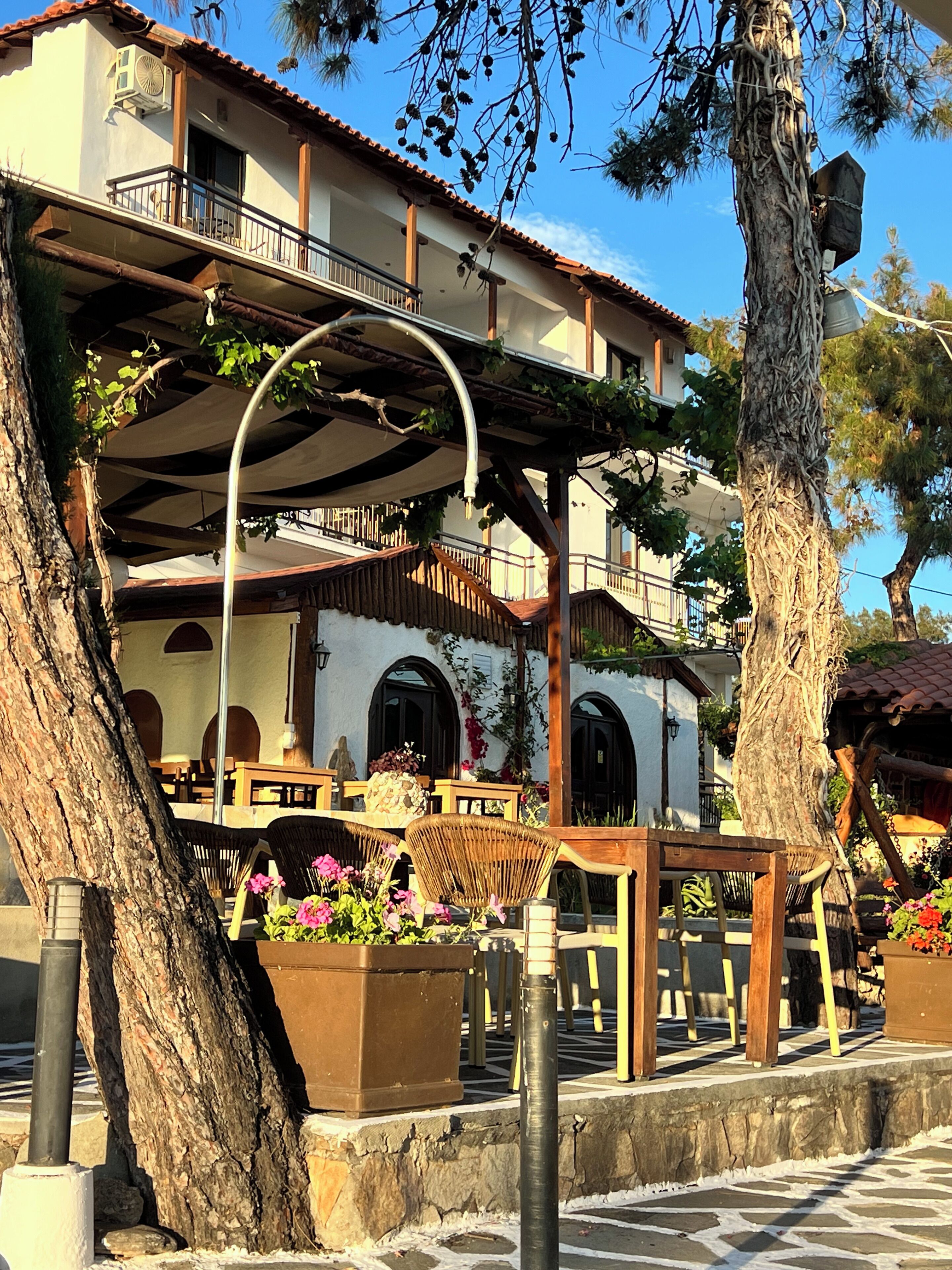 A building with a balcony, outdoor seating, and a tree.
