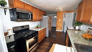 Een keuken met houten kastjes, roestvrijstalen apparatuur, een granieten aanrechtblad en een inbouwoven.