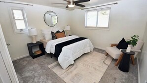 Een slaapkamer met een bed, nachtkastjes, een stoel, een plafondventilator en een raam.