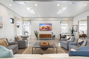 Ein modernes Wohnzimmer mit einer Sofagarnitur, einem Couchtisch, einem Essbereich und einem Gemälde an der Wand.