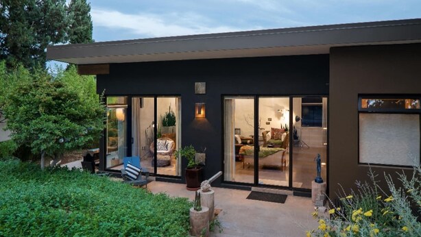 Una casa moderna con puerta de entrada de vidrio, un patio con mobiliario exterior y un jardín bien cuidado.