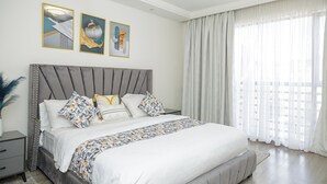 Ein modernes Schlafzimmer mit einem großen Bett, einem grauen gepolsterten Kopfteil und zwei an der Wand befestigten Kunstwerken.