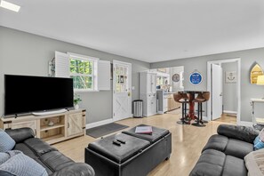 Ein modernes Wohnzimmer mit Flachbildfernseher, Ledersofas, einem Essbereich mit Tisch und Stühlen sowie einer Küche im Hintergrund.
