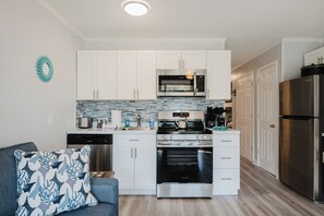 Cocina compacta con gabinetes blancos, microondas de acero inoxidable, horno y refrigerador.