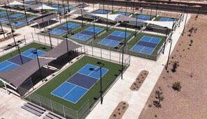 Un complesso di campi da tennis all'aperto con diversi campi, zone di copertura con posti a sedere e un'area circostante curata a giardino.