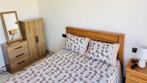 Ein Schlafzimmer mit einem Bett, einem Holzschrank und einem Nachttisch mit Lampe und Fernbedienung.