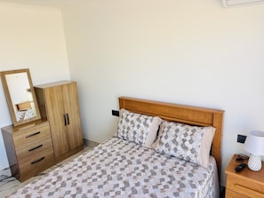 A bedroom with a bed, wooden wardrobe, and a nightstand with a lamp and remote control. - Mindelo's Brand New, Modern and Cozy: Family-Friendly Central Apartment for You! (Mindelo)
