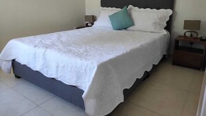 A neatly made bed with a white bedspread and pillows, two bedside tables with lamps, and a plain wall. - Apartasol La Tebaida, Quindío (La Tebaida)
