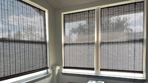 Ein Zimmer mit Fenster, Jalousien, einem Bücherregal mit Büchern und einem gemusterten Boden.