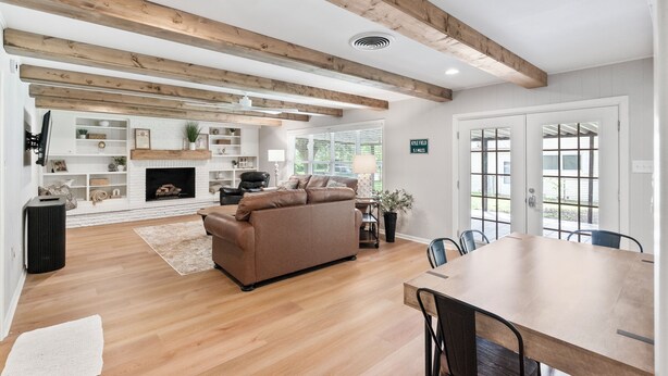 Un salón amplio con chimenea, vigas de madera, un sofá marrón y una mesa de comedor.