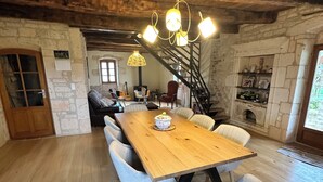 A rustic dining area with a wooden table and light blue chairs, a staircase, and stone walls.