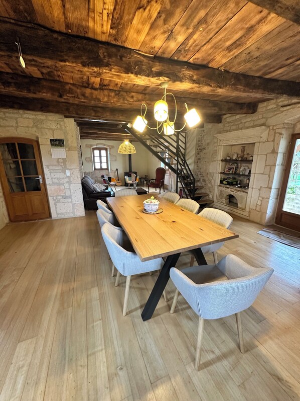 A rustic dining area with a wooden table and light blue chairs, a staircase, and stone walls.