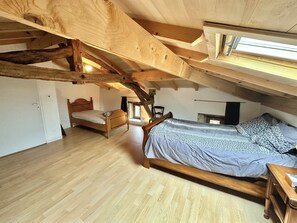 A bedroom with a sloped ceiling, wooden beams, a large bed, a smaller bed, and a window.