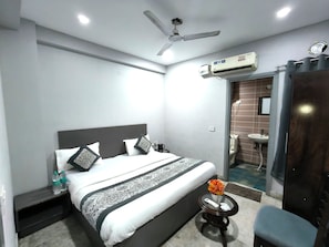 A hotel room with a bed, a ceiling fan, an air conditioning unit, a small table with a vase of flowers, and a bathroom visible through an open door. - Hotel White Stone near Anand Vihar  (New Delhi)