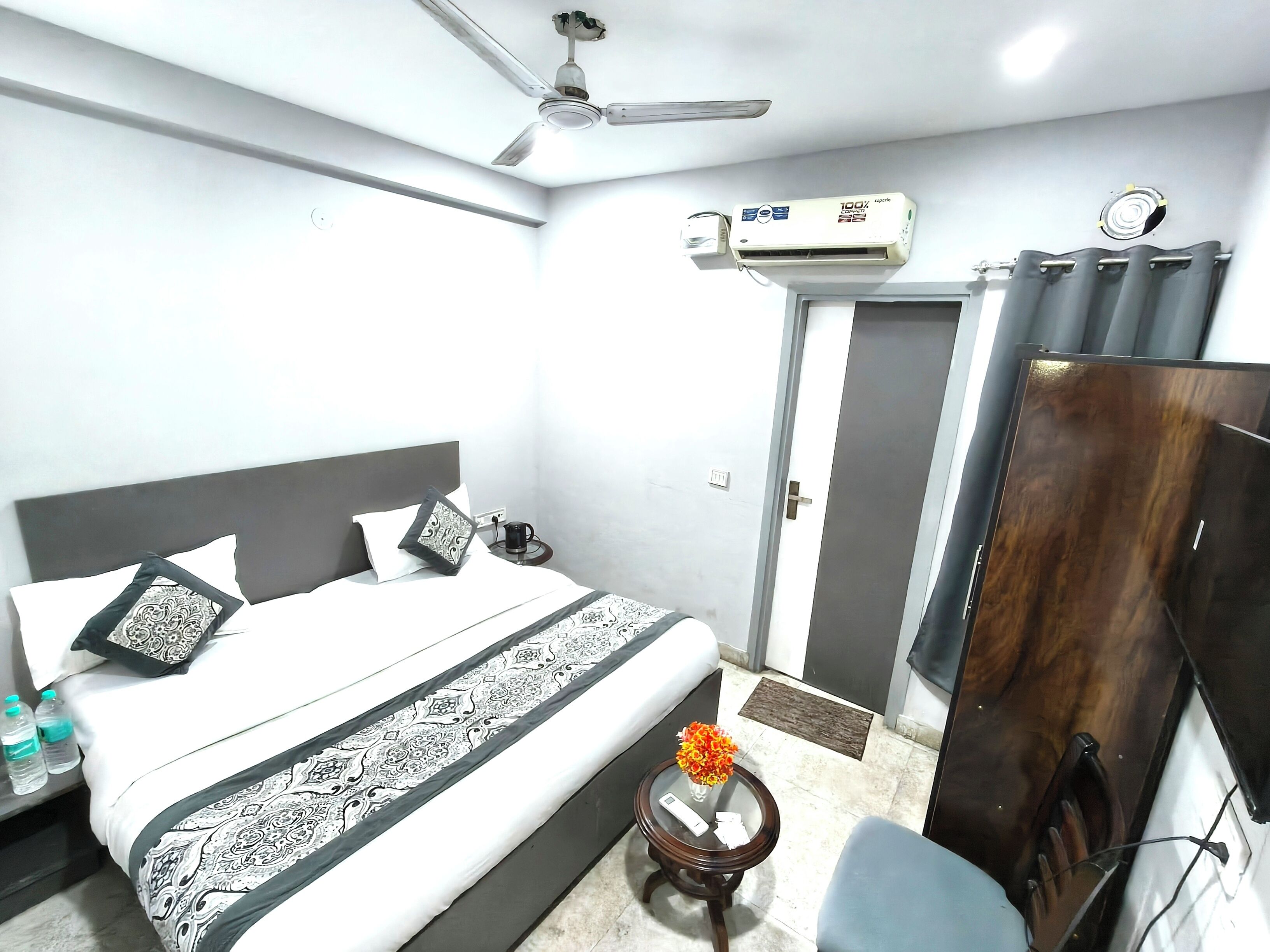 A hotel room with a bed, bedside table, nightstand, air conditioning unit, ceiling fan, and a wardrobe.