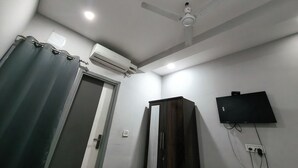 Een kamer met een plafondventilator, een airconditioningapparaat, een kledingkast en een tv aan de muur.