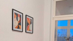 A modern living room with a gray sofa, two abstract paintings on the wall, a window with a view of trees, and a colorful rug on the floor. - Children welcome! Spacious family apartment 5 minutes from the center (Lübben (Spreewald))