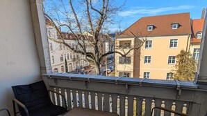 A balcony with a table and four chairs, a patterned rug, and a view of buildings and trees. - Children welcome! Spacious family apartment 5 minutes from the center (Lübben (Spreewald))