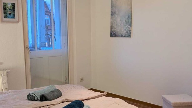 A bedroom with a large bed, a window, a painting, and a small table. - Children welcome! Spacious family apartment 5 minutes from the center (Lübben (Spreewald))