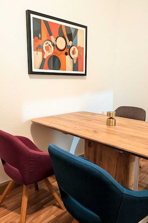 A dining area with a wooden table, two chairs, and a framed abstract painting on the wall. - Children welcome! Spacious family apartment 5 minutes from the center (Lübben (Spreewald))