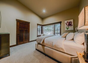 A bedroom with a large bed, a wooden door, a window with a view, and a painting on the wall. - Wilderness Club Manor For 20 (Eureka)