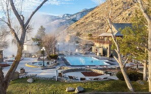 Un complejo de aguas termales con una piscina grande, zonas de descanso y montañas al fondo.
