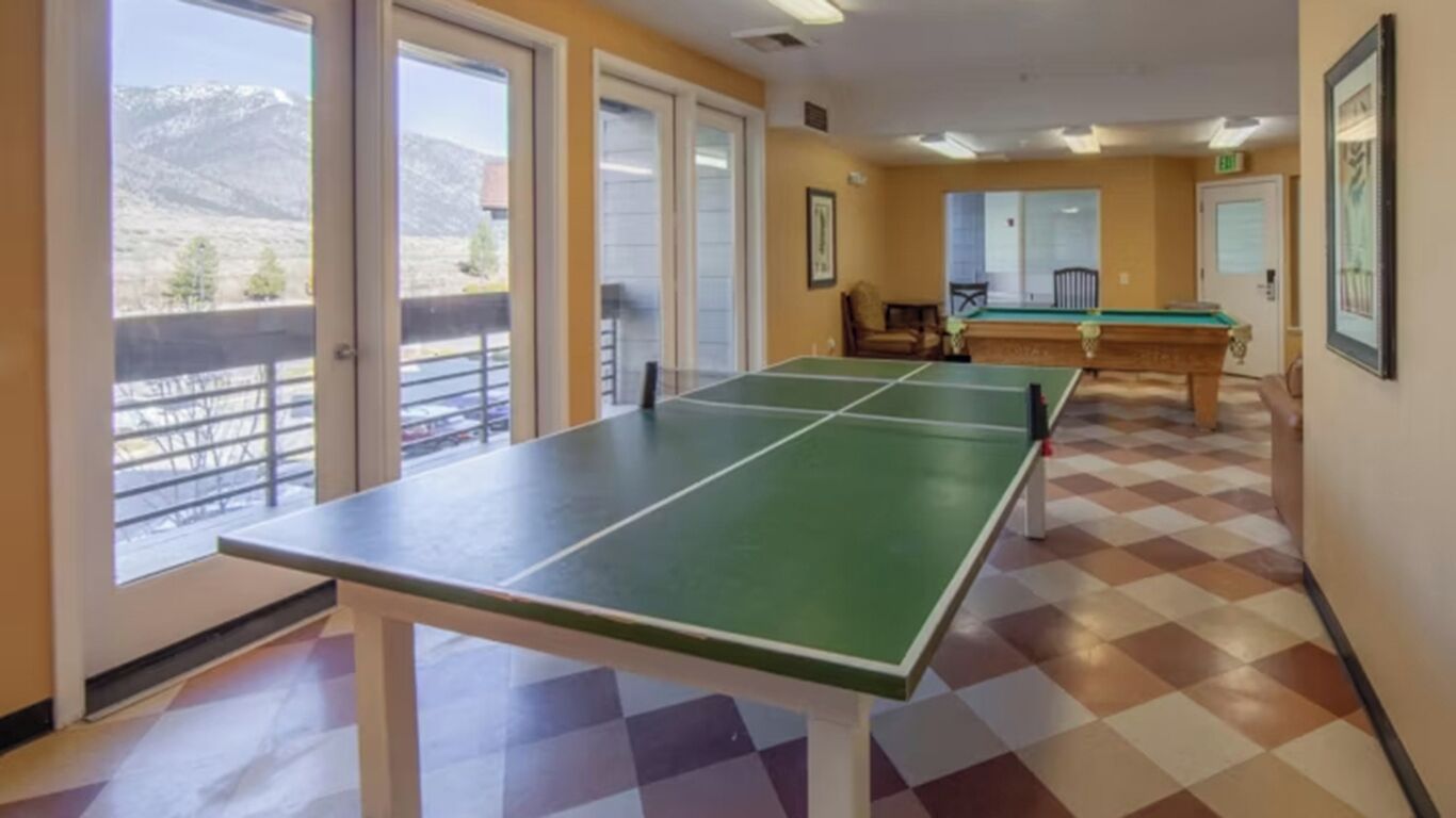 Una habitación con mesa de ping pong, mesa de billar y vistas a montañas a través de grandes ventanales.