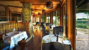A restaurant with wooden beams, stone pillars, and large windows offering a view of the outdoors. Tables are set with white tablecloths and wine glasses. - 1 Bedroom Villa, Heated Outdoor Pool and Hotsprings - Gorgeous mountain views (Genoa)