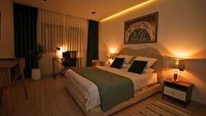 Une chambre d’hôtel avec un lit, des tables de chevet, un bureau, une chaise, une lampe, une plante et un tableau au mur.