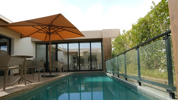 Une piscine dotée d’une paroi en verre, d’un espace salon extérieur et d’un grand parasol.