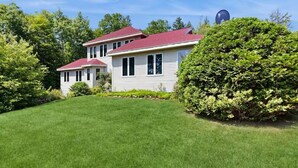A two-story house with a red roof, surrounded by green grass and trees. - Hilltop Family Escape | River Rock Fireplace (Naples)