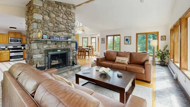 A spacious living room with a stone fireplace, leather sofas, a coffee table, and a dining area in the background. - Hilltop Family Escape | River Rock Fireplace (Naples)