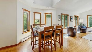 A spacious dining area with a wooden table and chairs, large windows, and a view of greenery outside. - Hilltop Family Escape | River Rock Fireplace (Naples)