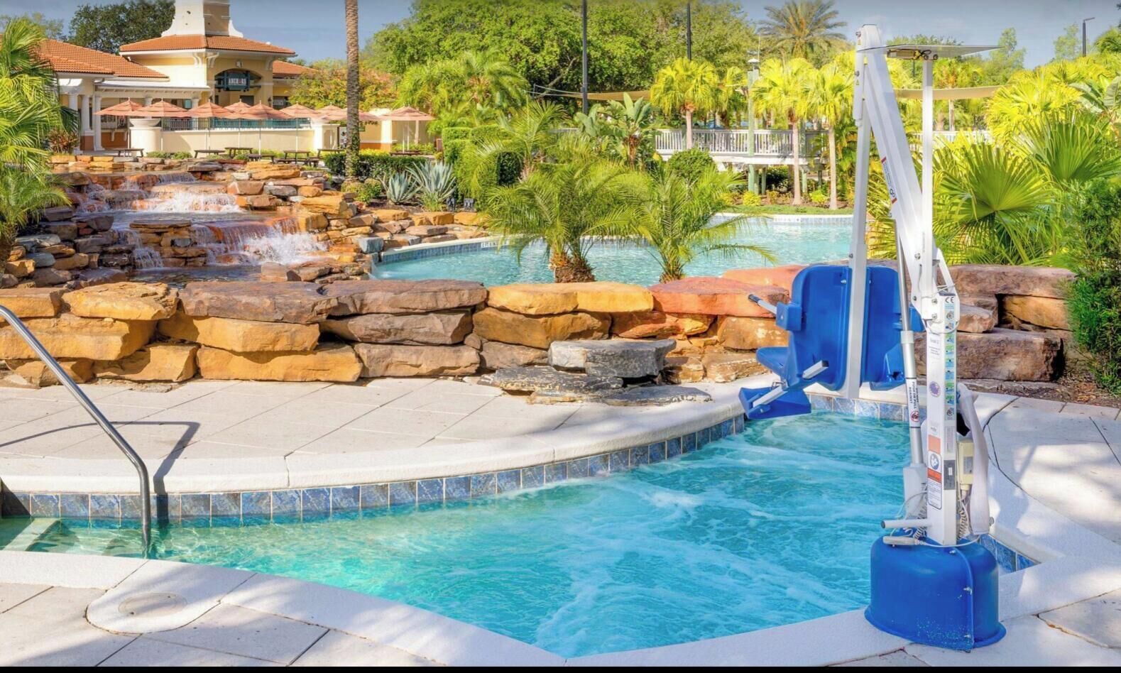 Zona de piscina con cascada, socorrista y área de descanso junto a la piscina.
