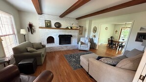 Una sala de estar con chimenea, dos sofás, un tapete estampado y un comedor al fondo.