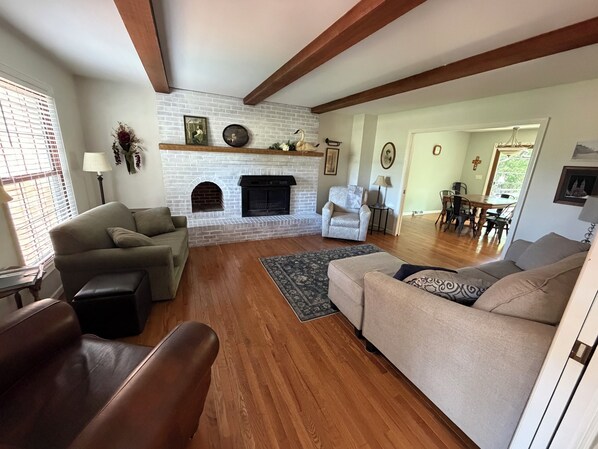 A living room with a fireplace, two sofas, a patterned rug, and a dining area in the background.