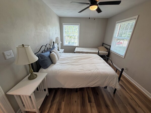 Une chambre à coucher avec un lit, des tables de chevet, un ventilateur de plafond et deux fenêtres.