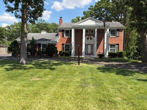 A two-story brick house with a front porch, a chimney, and a well-maintained lawn.