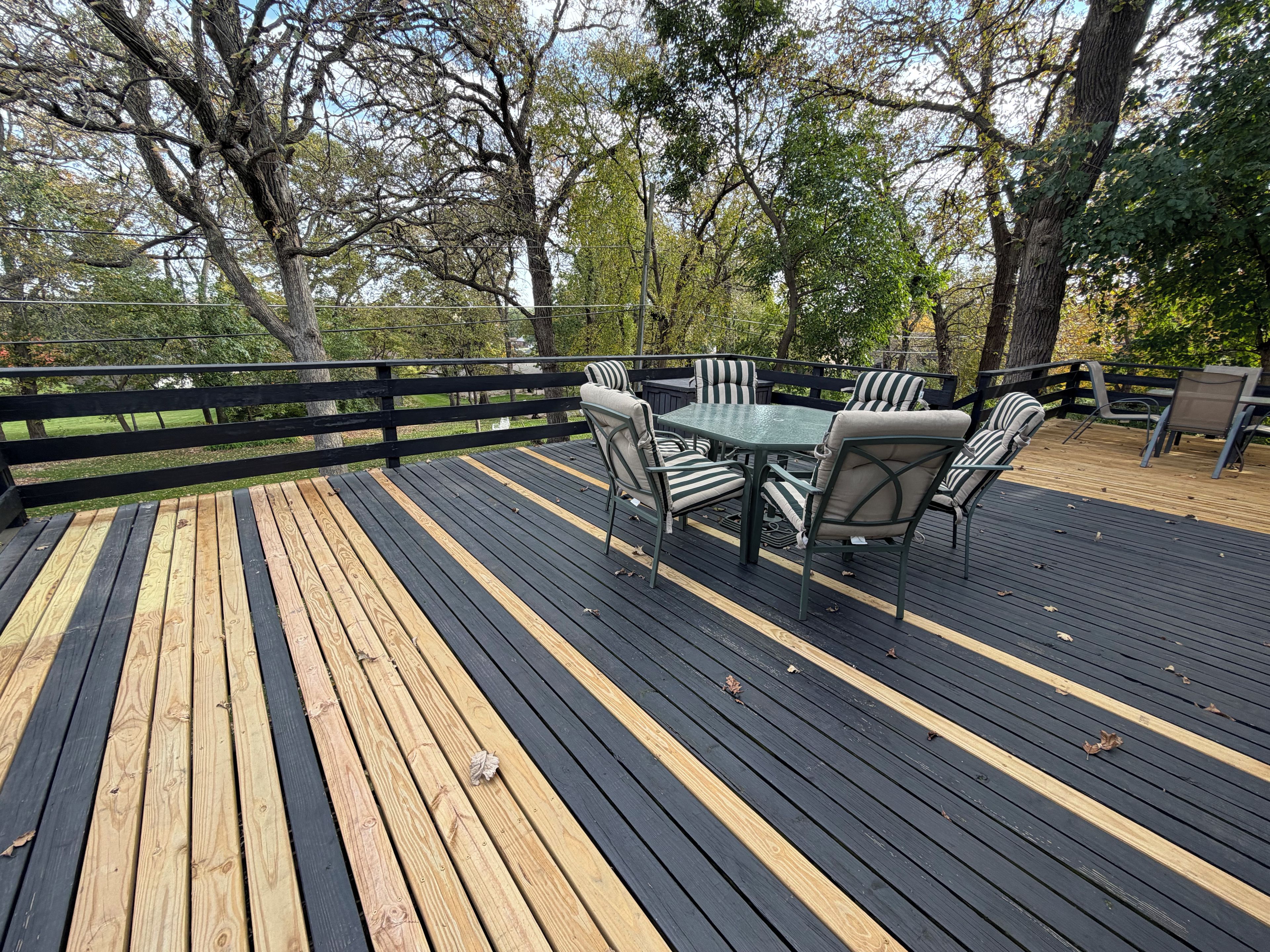 A wooden deck with a table and chairs, surrounded by a black railing.