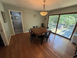 A dining room with a wooden table and chairs, a chandelier, and a view of a deck through a glass door.
