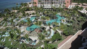 Ein Resort mit mehreren Schwimmbecken, Palmen und einem großen Hotelgebäude im Hintergrund.