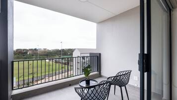 A balcony with a view of a sports field, a potted plant, and two chairs.