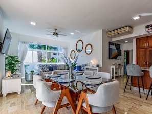 A modern dining area with a glass-top table, grey upholstered chairs, and a ceiling fan.