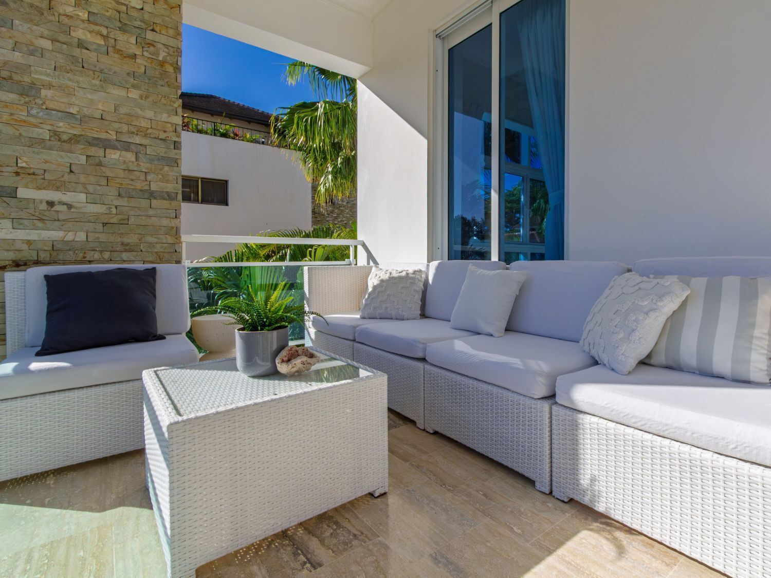 A balcony with a white wicker sofa, a small table, and a potted plant.