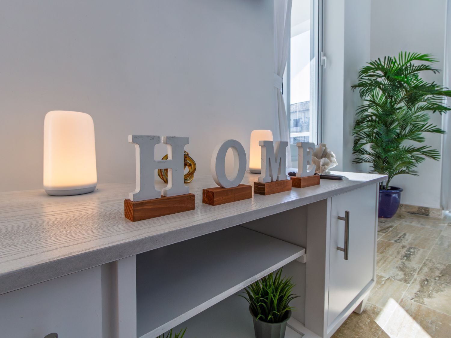 A modern interior with a white console table displaying illuminated letters spelling "HOME" and a decorative plant.