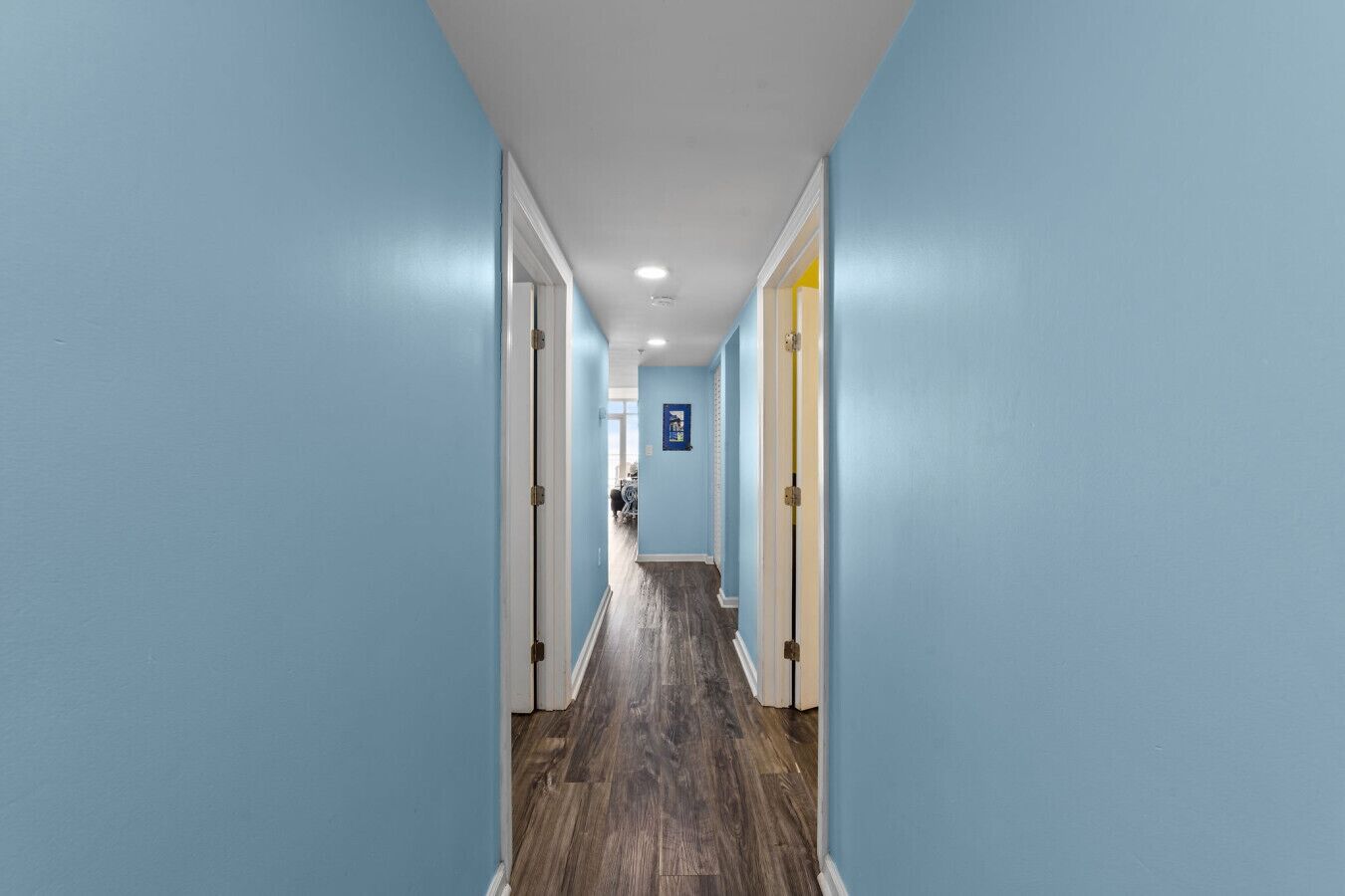 A hallway with light blue walls, wooden flooring, and white doors.
