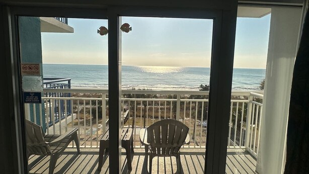 Un balcon avec vue sur l’océan, une table et deux chaises.